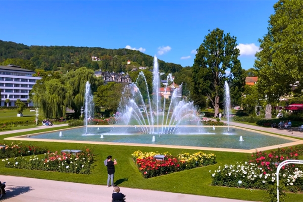 Ein Wasserbecken mit Fontänen umgeben von Wiese und Blumen im Kurpark Bad Kissingen.